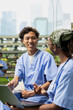 © DC Studio - Medical students smile while discussing handwritten notes beside a laptop on a campus bench, sharing ideas through peer tutoring during healthcare study.