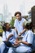 © DC Studio - Diverse medical students in blue scrubs share notes and discuss coursework on a laptop while sitting on a campus bench, collaborating on healthcare training during an outdoor study session.