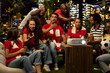 © DC Studio - Football fans react passionately while watching a decisive soccer match projected onto a screen on a rooftop terrace, shouting during a tense live sports broadcast with fellow supporters.
