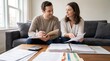 © AspctStyle - Young couple reviewing financial documents and bank statements on a living room sofa, practicing responsible budgeting and tax preparation for home ownership and family mortgage planning.