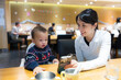 © leungchopan - Asian mother and toddler boy looking at smartphone at restaurant table