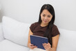 © leungchopan - Woman sitting on white sofa reading tablet in living room