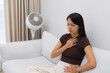 © leungchopan - Woman holding hand on chest having heartburn symptom on couch