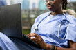 © DC Studio - Female medical student in blue scrubs with a stethoscope types notes on a laptop while sitting on a campus beanbag for a healthcare study session.