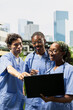 © DC Studio - Medical students in scrubs work together over laptop notes outdoors on campus, discussing medical school coursework and sharing ideas during a relaxed collaborative group study session.