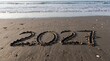 © Hastock - 2027 year written in sand on a beach with ocean waves in background.