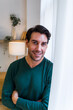© Metadancer - White man smiling indoors by curtain with crossed arms