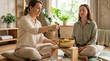 © Angavlan - Woman demonstrating singing bowl therapy for client, fostering calm in a tranquil room. Session uses a golden brass bowl and mallet, promoting deep relaxation.