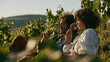 © rabbit75_fot - a woman sit in a vineyard, sipping wine. The man, with curly hair, wears a green shirt and brown pants. The woman, wearing a white blouse, has curly hair. They are surrounded by lush green grapevines.