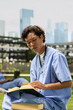© DC Studio - Medical student, textbook and scrubs as a learner reads with a stethoscope around the neck. Healthcare training, knowledge and academic study support medical education on an outdoor campus lawn.