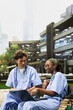 © DC Studio - Medical students, laptop and teamwork as peers in scrubs review digital material together on a bench. Collaboration, education and knowledge sharing support group learning in an outdoor campus garden.