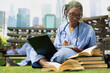 © DC Studio - Medical student, notebook and laptop as a learner in scrubs writes study notes beside open books on grass. Healthcare education, concentration and study skills support independent learning on campus.