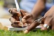 © DC Studio - Handwriting, notebook and pen as a student writes medical study notes on grass in close-up. Learning, concentration and medical education relate to academic practice on an outdoor campus lawn.