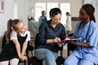 © DC Studio - Signature, paperwork and nurse with woman signing medical form on clipboard as young girl watches in waiting area, for registration, administration, patient support and healthcare service.