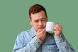 © Pixel-Shot - Toothache and dental pain, young man suffering from sensitive teeth while holding a hot cup of coffee or tea on a green background