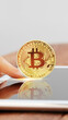 © fotofabrika - Bitcoin coin held over a tablet screen in a bright space during the day