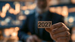 © jainul - Businessman holding wooden block with year 2027 in office setting with financial charts