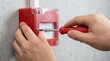 © Gibster - Fire alarm system emergency maintenance service with technician hand using screwdriver on red safety device on concrete wall