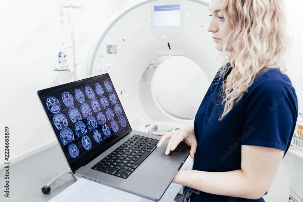 Female radiologist holding a laptop displaying brain MRI scans beside ...