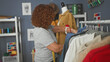 © Krakenimages.com - Woman arranging garments on a rack, touching denim and knits while wearing a measuring tape and a wrist pincushion in a sewing studio; focused craft.