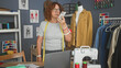 © Krakenimages.com - Woman holding smartphone with measuring tape around her neck while checking messages at sewing table in design studio; creative concentration.