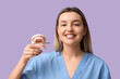 © Pixel-Shot - Dental health and oral hygiene education, smiling dentist holding a jaw model with implant for patient consultation on a solid purple background