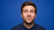 © AiStock B - Man making funny face grimace looking up against blue background portrait