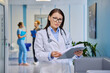 © Valerii Honcharuk - Mature female doctor holding clipboard in modern clinic hallway portrait