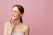 © SHOTPRIME STUDIO - Smiling woman with pink facial cream on her cheek, pink background. Clear concept of skincare, wellness, and self care. Soft studio lighting creates a warm, calming mood and a fresh beauty routine