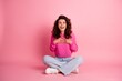 © deagreez - Happy woman in pink sweater sitting cross-legged on pink background smiling with hands on chest expressing surprise and joy in casual studio portrait