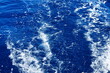 © DIgnat_Switzerland - Deep blue ocean surface with turbulent boat wake and white foam from top-down viewpoint, textured water ripples and sunlit highlights suitable for marine and travel use cases