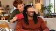 © olegganko - Woman covering her seated partner eyes while holding a red card in a warm living room