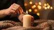 © Ariel - Woman's hands lighting a cream pillar candle with a wooden match in a cozy room with warm fairy lights bokeh, ideal for hygge, autumn and winter lifestyle content.