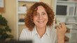 © Krakenimages.com - Middle aged woman removing eyeglasses while smiling at a computer screen in an office with shelves, boxes and a plant; contentment approachability.