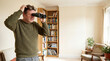 © VektorDesign - Man searching living room with binoculars while scratching head in a humorous everyday scene