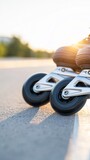 Inline skates rolling over sunlit asphalt at golden hour, with black wheels and silver frames casting long shadows outdoors