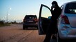 © Fei - Woman making an emergency phone call leaning against a damaged car after a traffic accident on a highway at dusk, seeking help or insurance assistance.