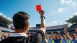 © miss irine - Pro soccer referee shows bright red card to player in large stadium. Official makes disciplinary decision during intense football match. Angry crowd, players react to foul in sunlit arena. Referee