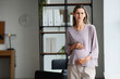 © Pixel-Shot - Pregnancy stress and workplace anxiety, pregnant woman feeling worried or overwhelmed while standing in a modern office environment