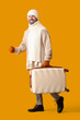 © Pixel-Shot - Winter travel and vacation planning, smiling man in warm sweater and scarf carrying suitcase for holiday trip on yellow background