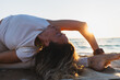 © Martí Rosselló - Woman practicing a reclining yoga stretch on a beach at sunset