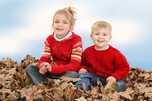 brother and sister sitting in pile of leaves
