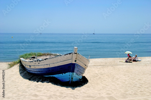 old rowing boat on white sandy beach and people sunbathing next
