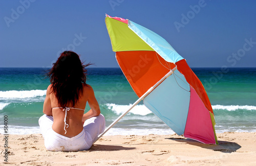 woman sitting under colorful parasol on white sandy beach