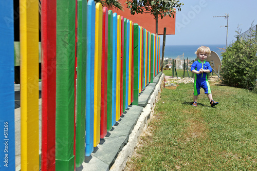young boy walking beside colourful fence in the summer
