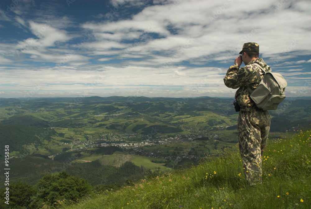 khaki tourist with binoculars is looking in villag