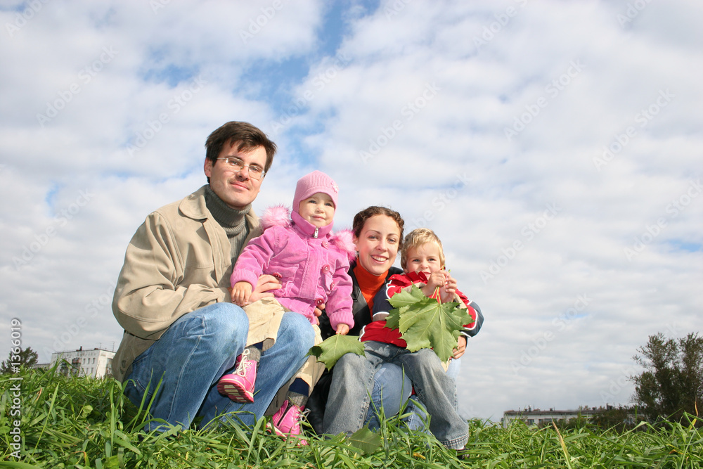 family of four sit. clouds. grass family of four sit. clouds. grass