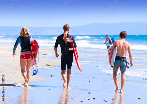 three young surfers walking on beach ~ image for editorial use o