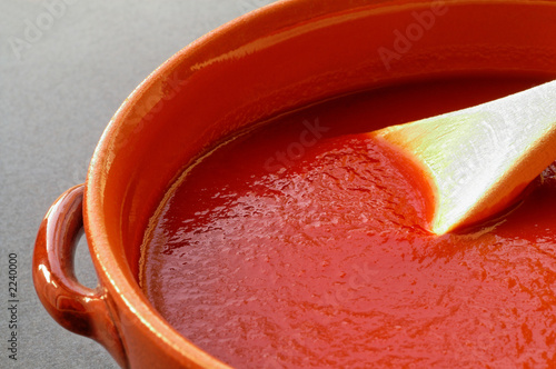 terracotta pot and wooden spoon with tomato sauce.