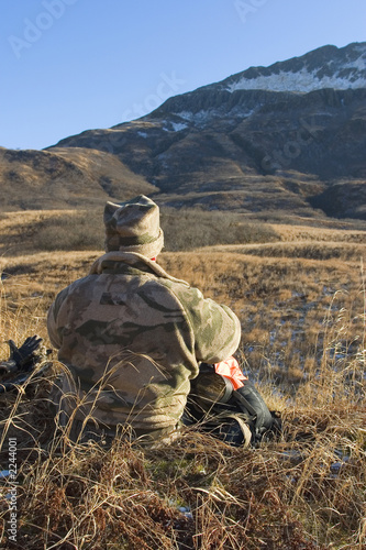 camo hunter watching the hillside closely with snow on top of the peaks